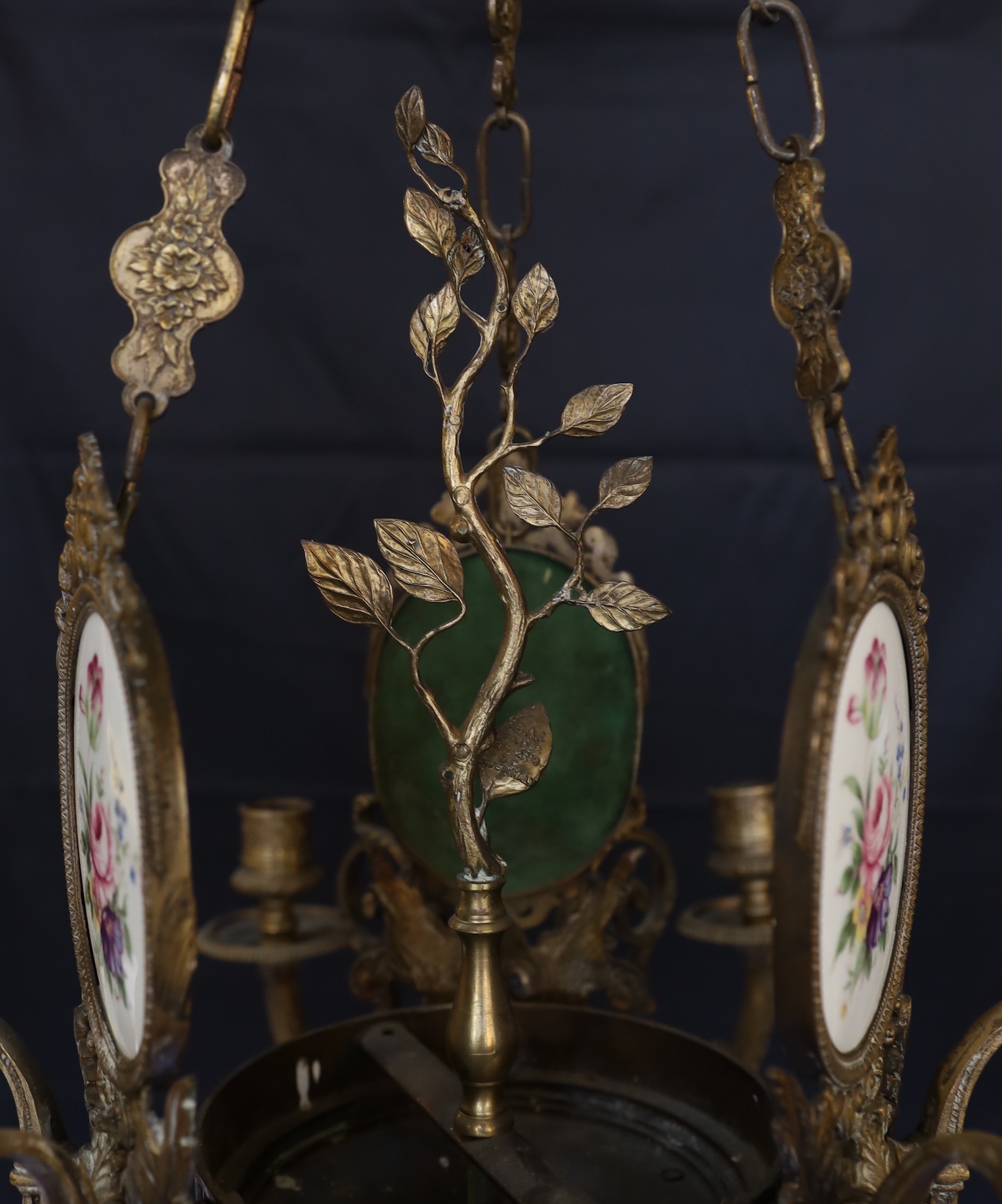 A 1930s English bronze and porcelain six light chandelier with central foliate stem and three oval porcelain plaque decorated with flowers, height 79cm. width 55cm